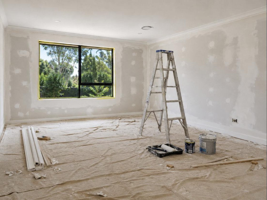 Before — the same lounge mid-renovation with drop sheets, a ladder, paint tins and construction dust